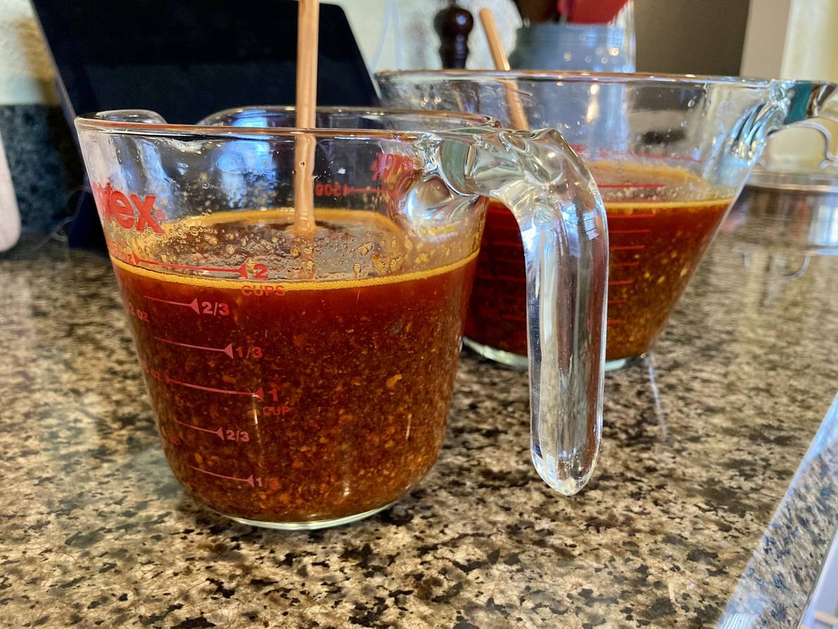 2 measuring cups full of a red liquid and a whole bunch of chili flakes.