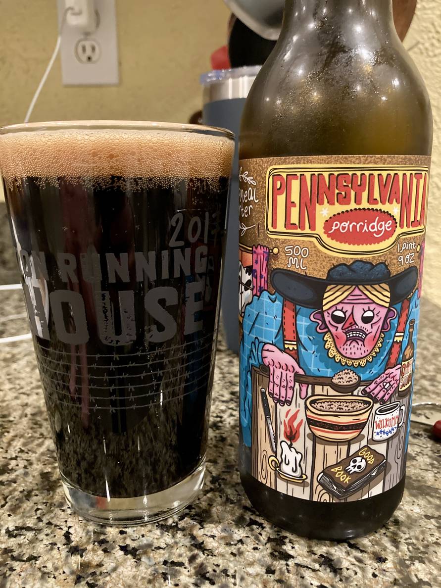 A beer glass full of dark beer sits on the counter. Next to it is a beer bottle. The label says “Pennsylvania Porridge” with a highly stylized illustration of a woman eating a bowl of oatmeal.