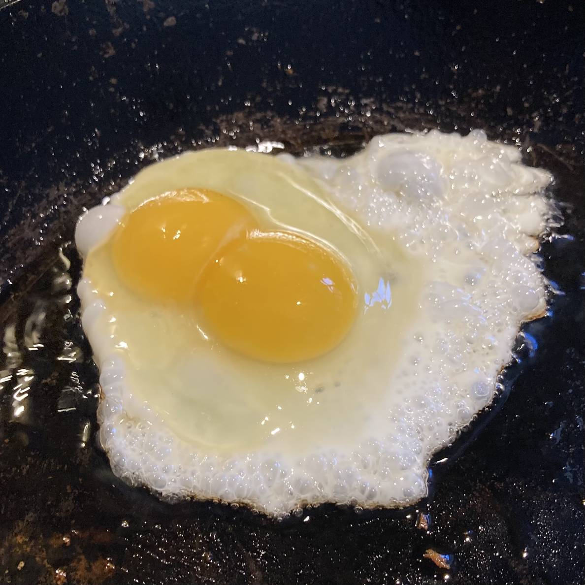 An egg cooking in a frying pan with two yolks.