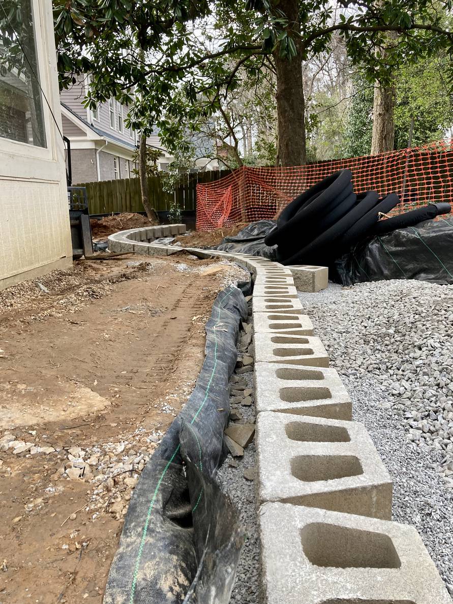 A line of wall blocks in a ditch with crushed stone extends from the right foreground into the background.