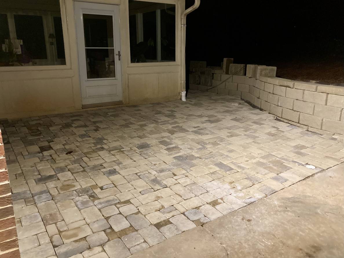 A sun porch with paver stone in front of it. A retaining wall borders the pavers and goes beyond the sun porch.