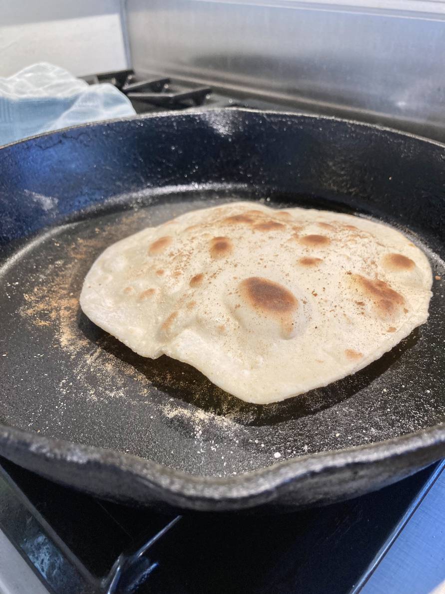 A cast iron skillet on a stove with what looks like a tortilla in it, but it’s two Mandarin pancakes cooking.