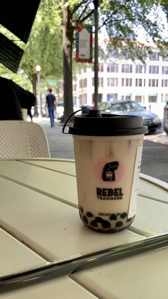 A cup of bubble tea sits on an outside table. A city street is in the background.