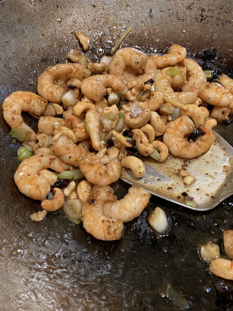 Stir-fried shrimp with cashews, green onions, and sauce in a wok with a wok spatula.
