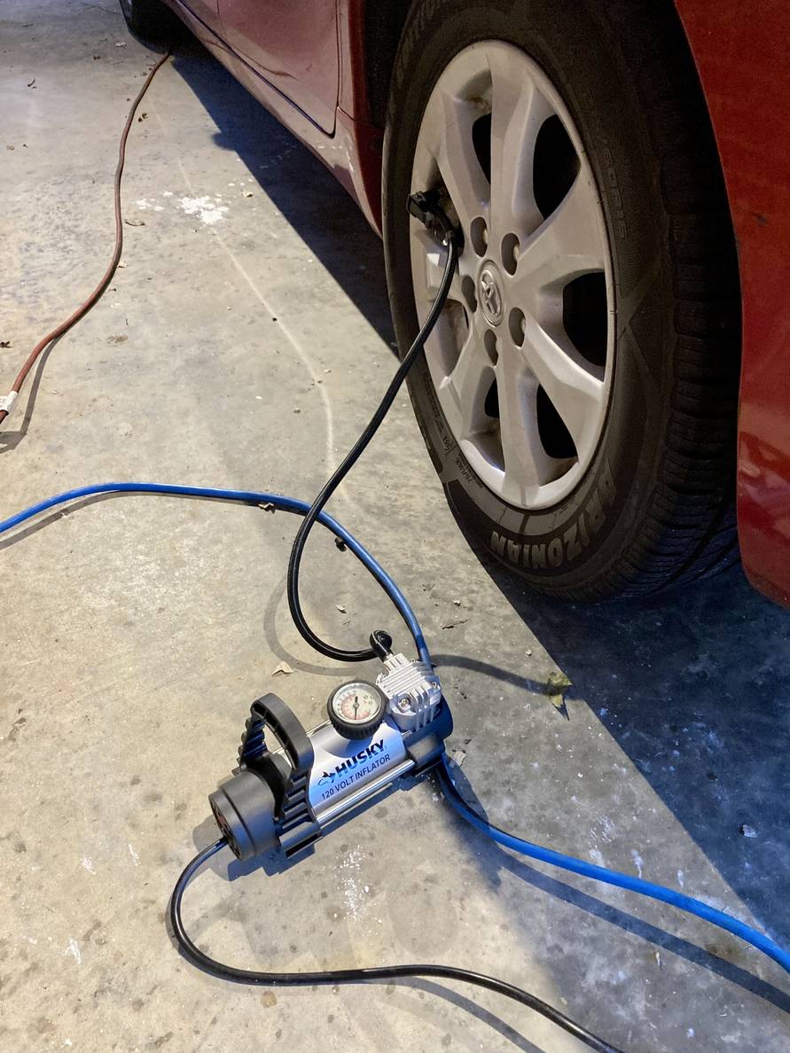 A small electric pump sits on the ground in a residential carport. The hose is connected to a car tire.