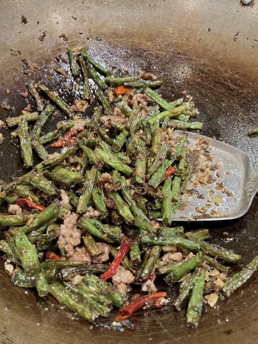 Charred green beans, chilis, and aromatics in a wok with a wok spatula.