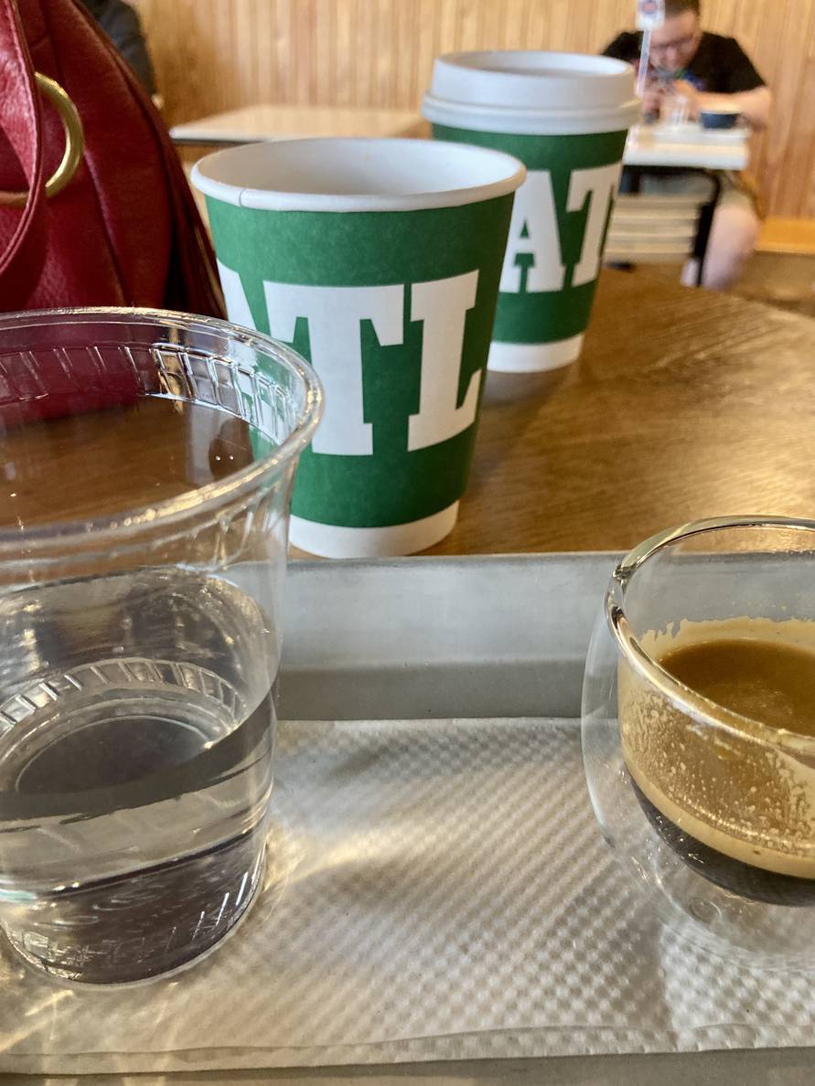 An espresso and two to-go cups of coffee on a table.