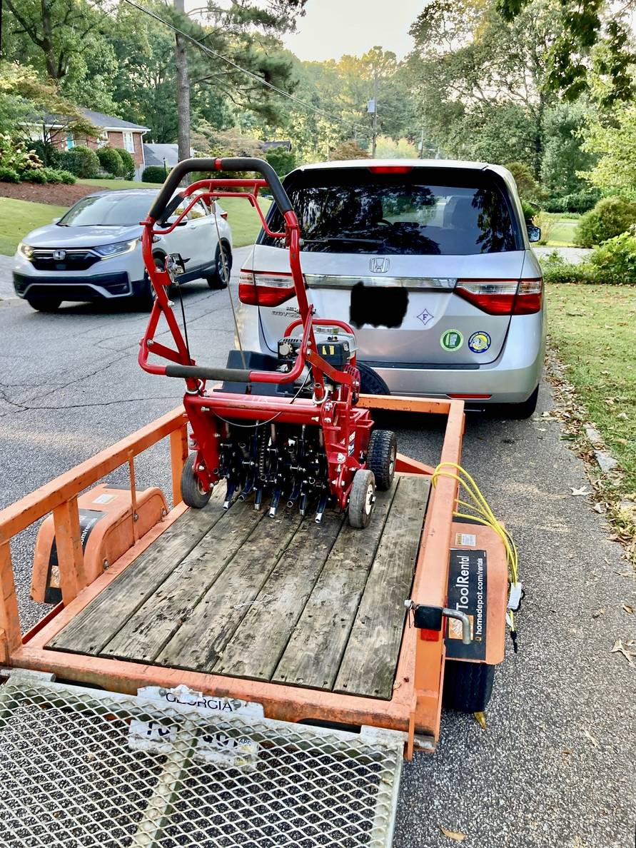 An aerator in a small rental trailer hitched to a minivan.