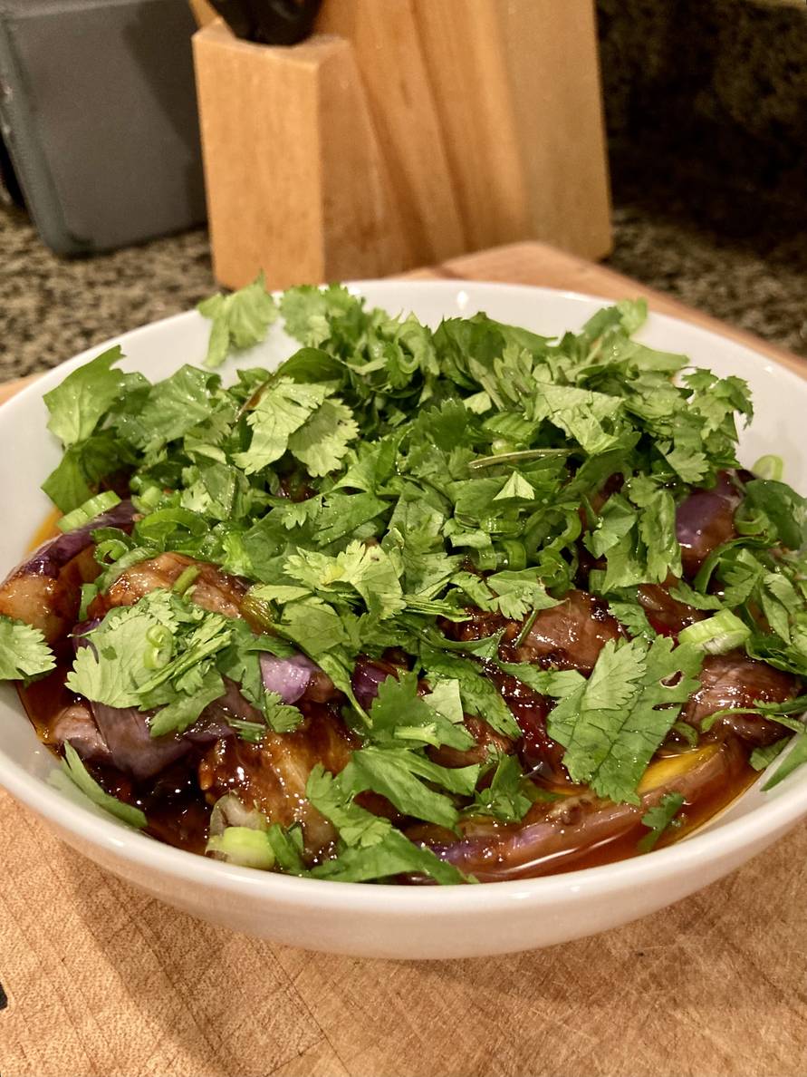 A bowl of eggplant planks in sauce topped with cilantro and green onions.