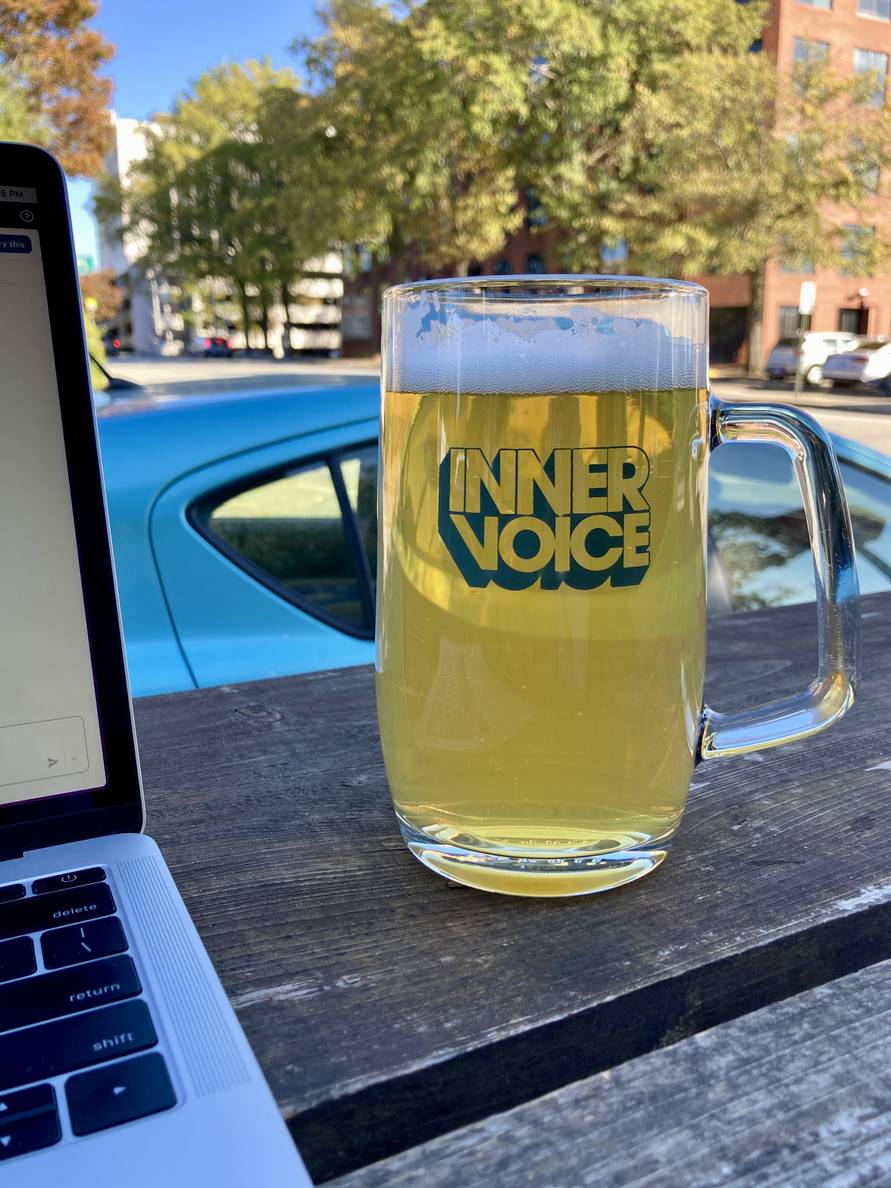 A mug of beer on an outdoor wooden bar. The mug says “Inner Voice.”