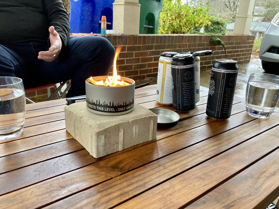 A small outdoor firepit on a table with beer cans behind it