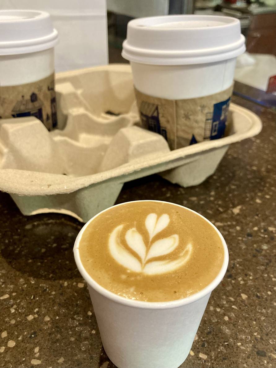 A macchiato with milk art in a to-go cup on a counter.