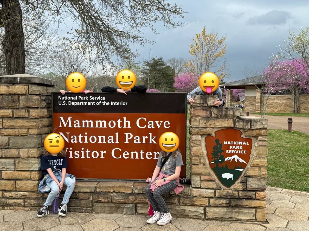 Kids sit in front and on top of the a sign that says “Mammoth Cave National Park Visitor Center.”