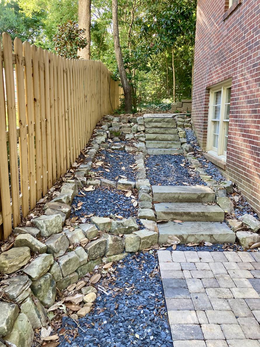 Steps go up alongside a house. The bulk of it is stone, but there are small areas of mulch.