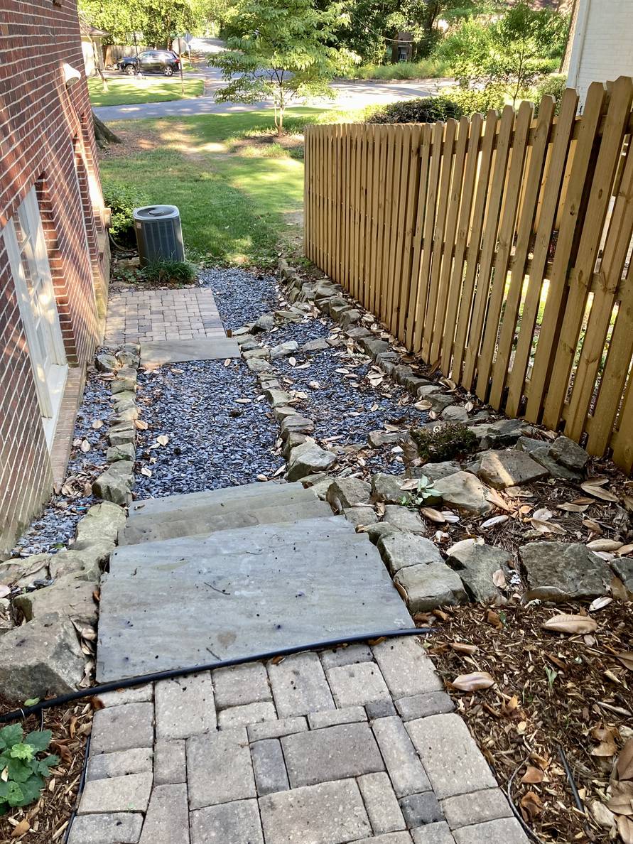 Steps go down alongside a house. The bulk of it is stone, but there are small areas of mulch.