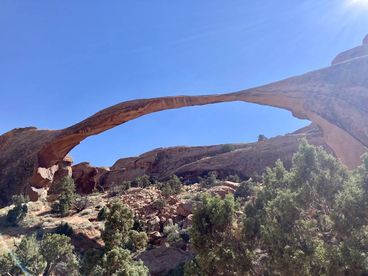 A thin stretch of stone creates a wide arch. Some sky and some mountain are visible through the arch.