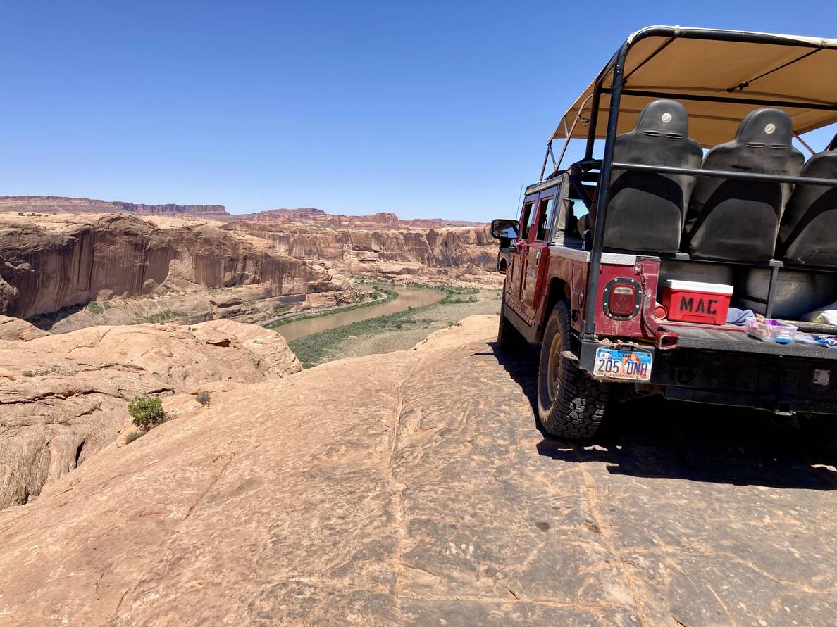 A hummer sits atop a stone ledge. Cliffs and bluffs are in the distance and a river runs through a valley below.