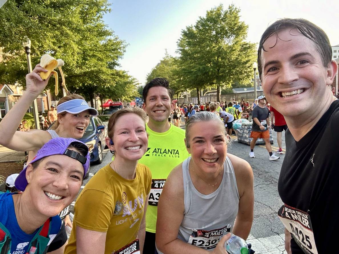 A group of sweaty men and women smiling at the finish of a running course.