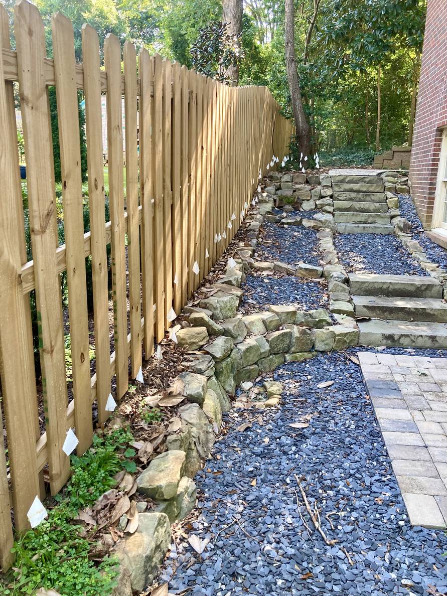 Steps between a fence and a house. Most of the ground is stone and slate chips, but a narrow area long the fence and slightly wider in the distance have white flags every square foot.