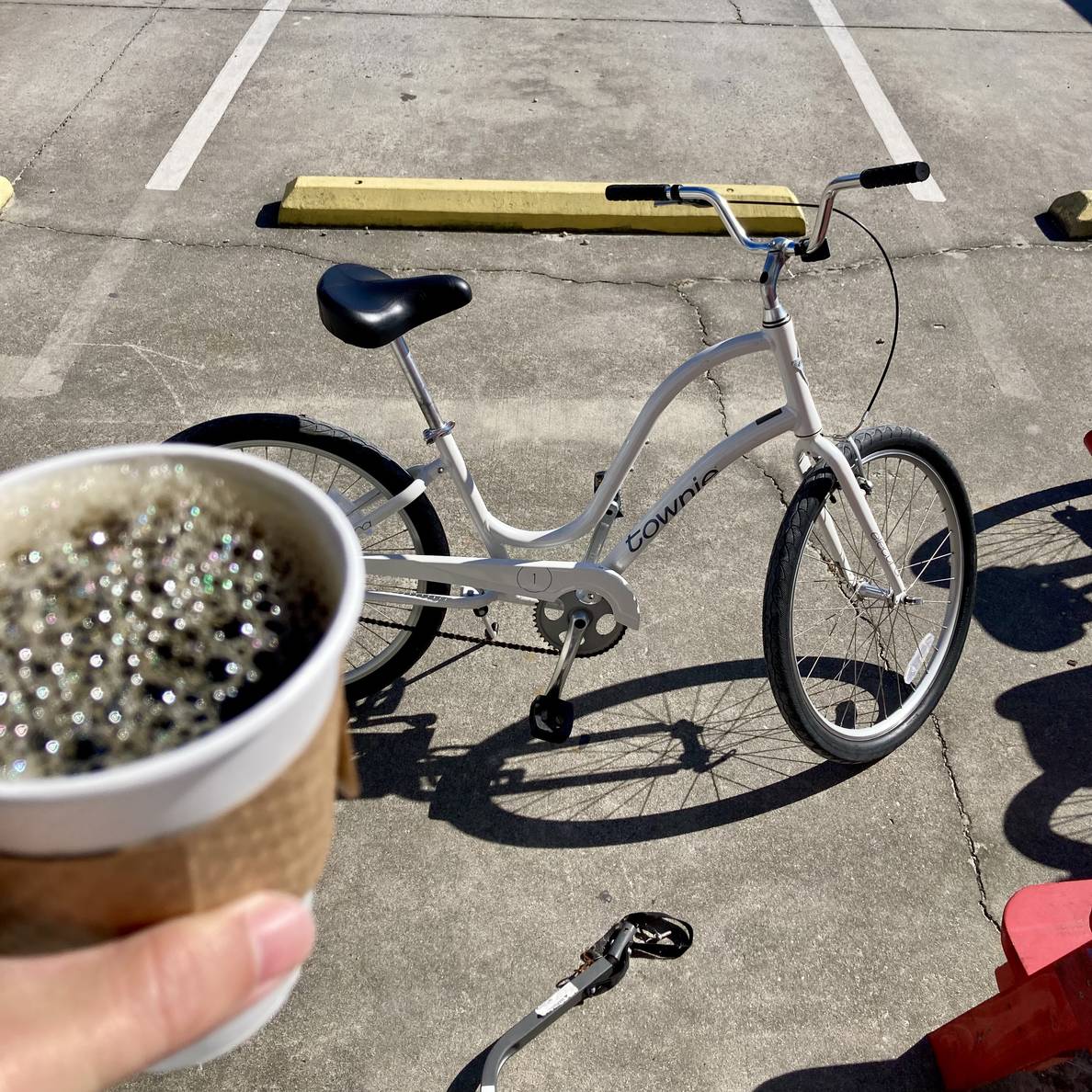 A hand holds a cup of coffee. Behind it is a bicycle.