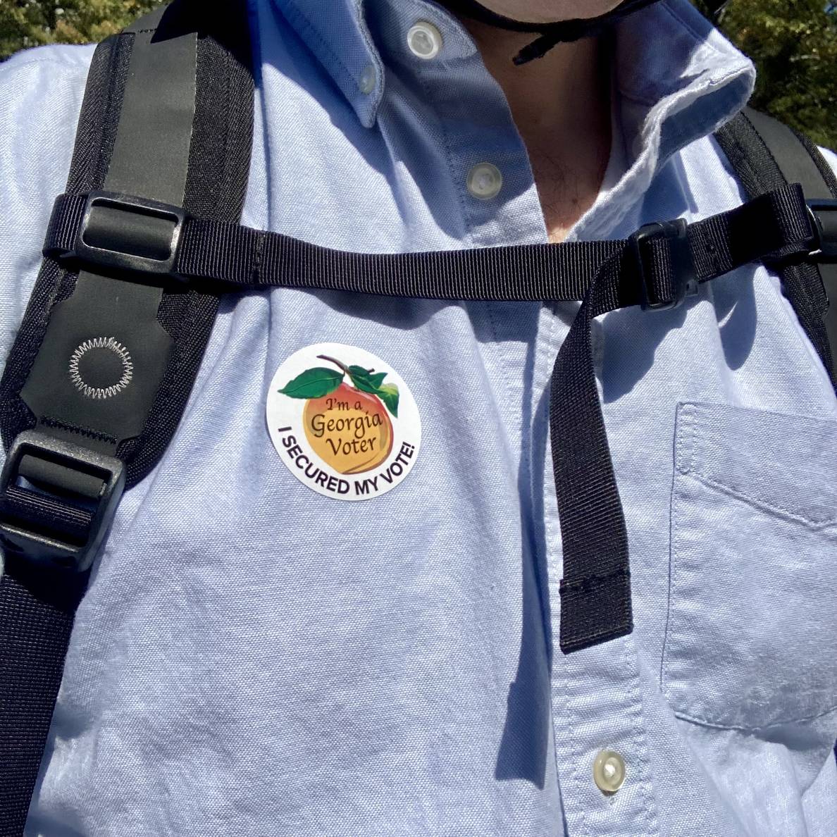 Close up of a person’s shirt with a sticker that says “I’m a Georgia voter. I secured my vote!” The person is wearing a backpack and a bicycle helmet.