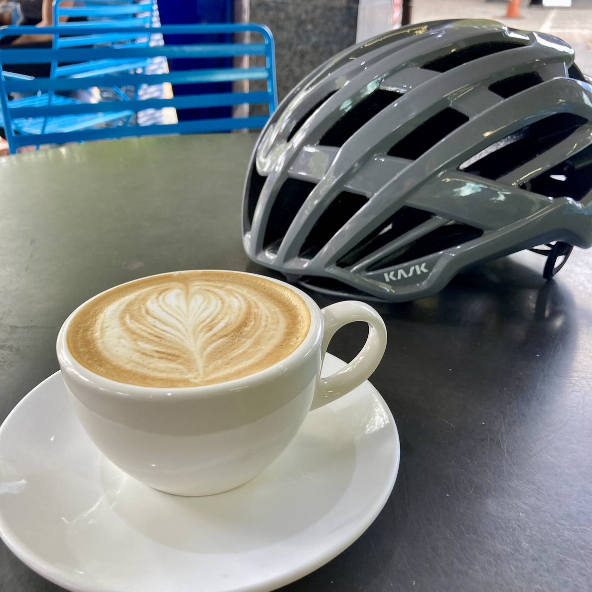 An outdoor table with a cappuccino and a bike helmet.