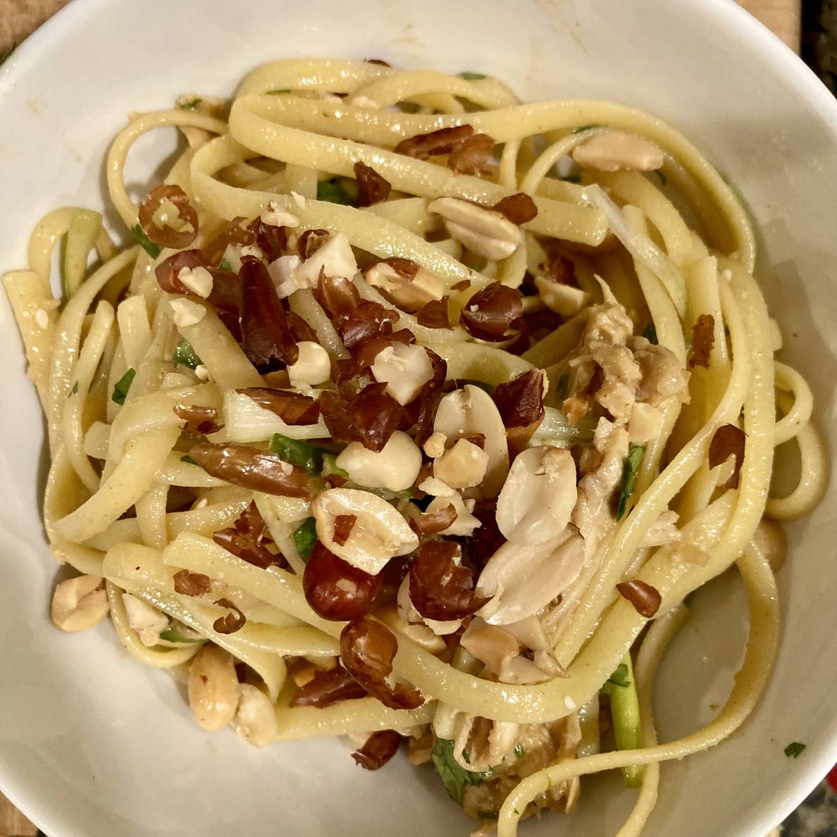 A bowl of noodles topped with peanuts. Bits of chicken and slivers of vegetables are visible.