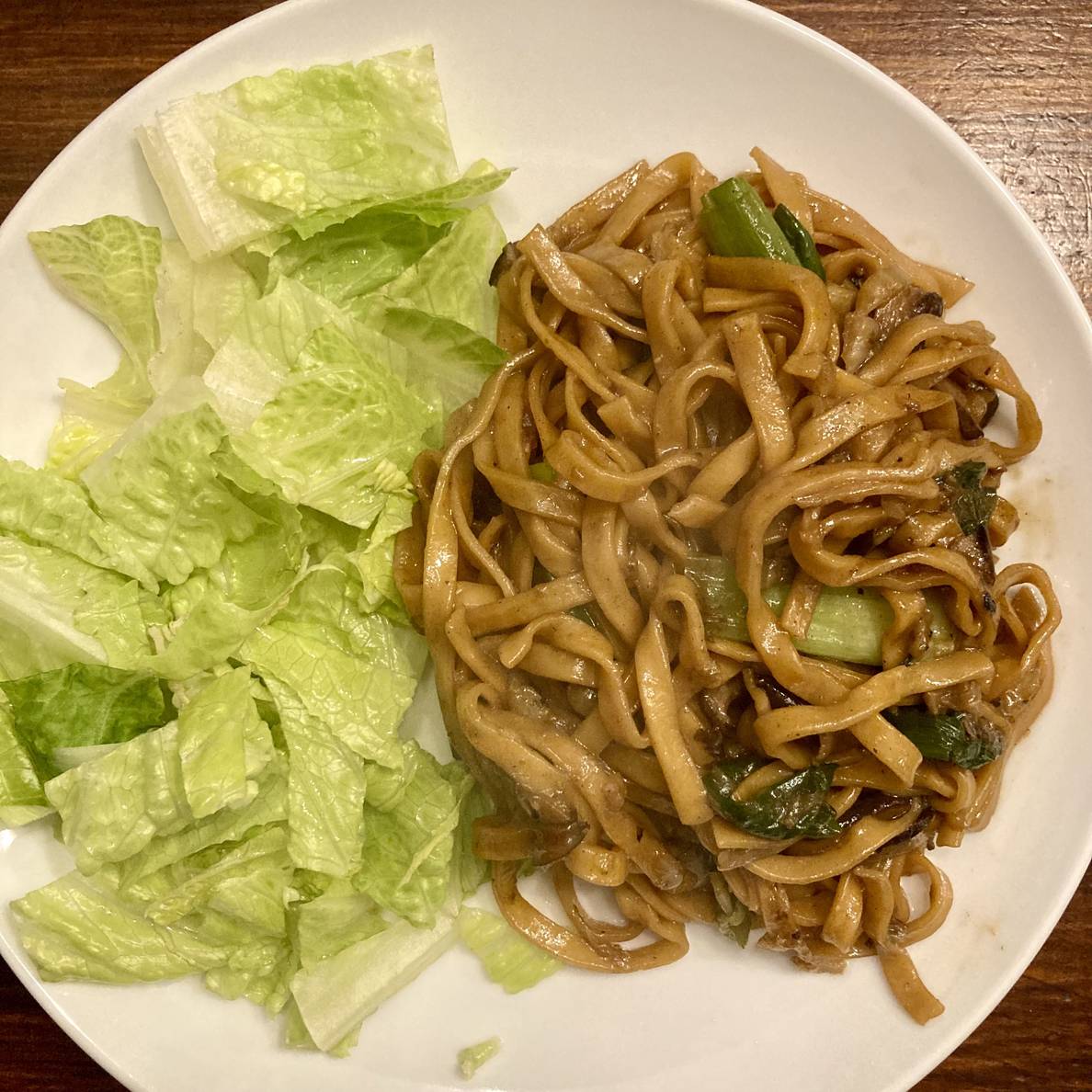 A plate on a table with half torn lettuce and half a noodle dish with bits of scallion visible.