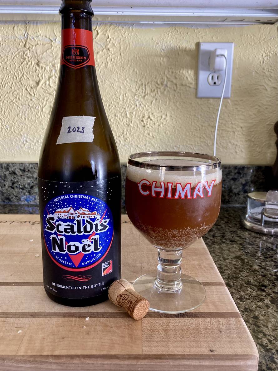 A 750ml bottle of Scaldis Noël with a piece of tape with the year “2023” marked on it. Next to it is a Chimay chalice filled with beer.