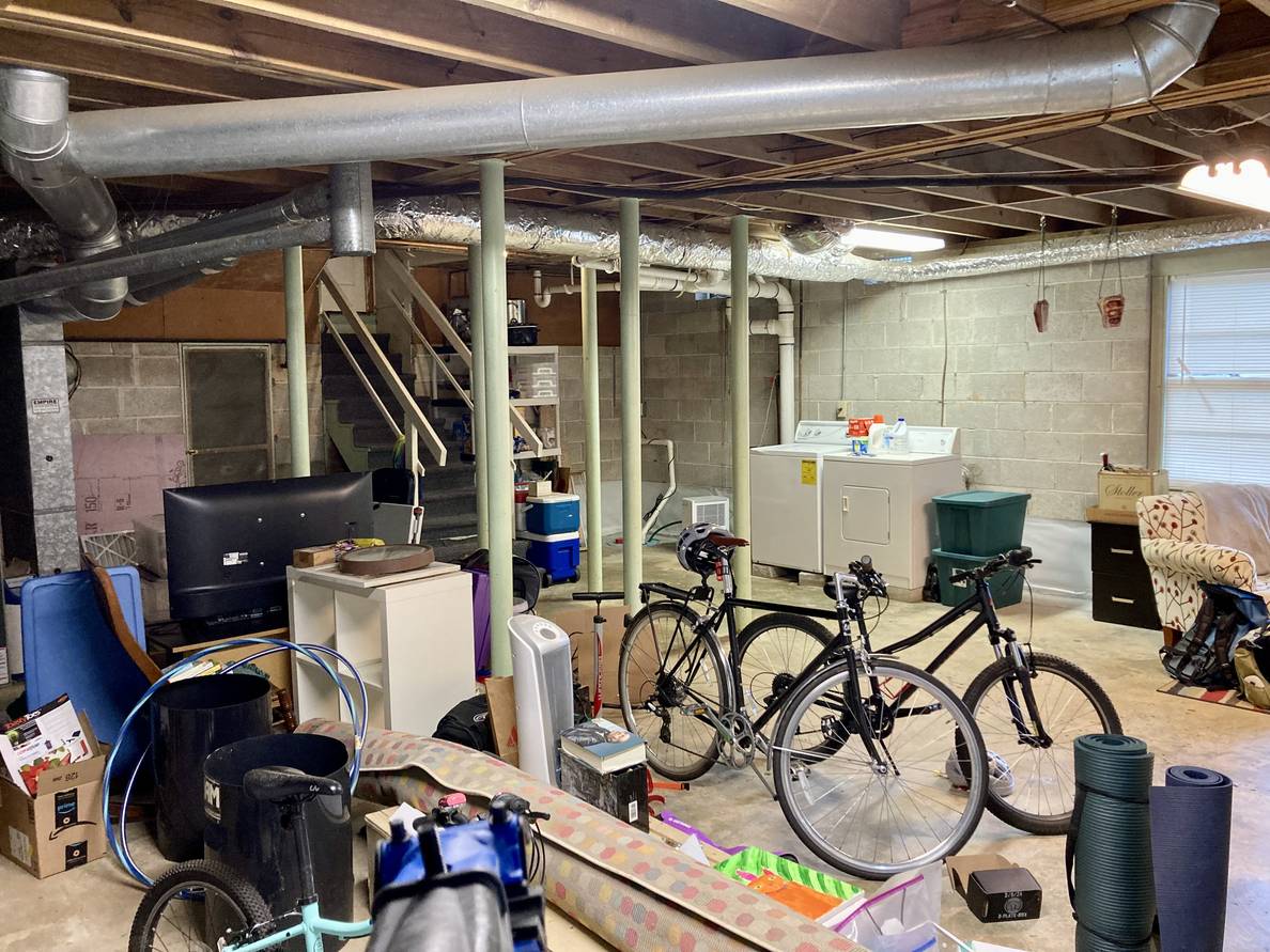 An unfinished basement with bicycles, stuff on the ground, and laundry machines.