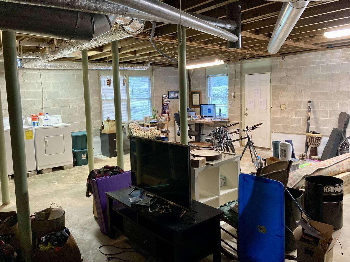 An unfinished basement with bikes, a bunch of stuff, laundry machines, and a computer desk.