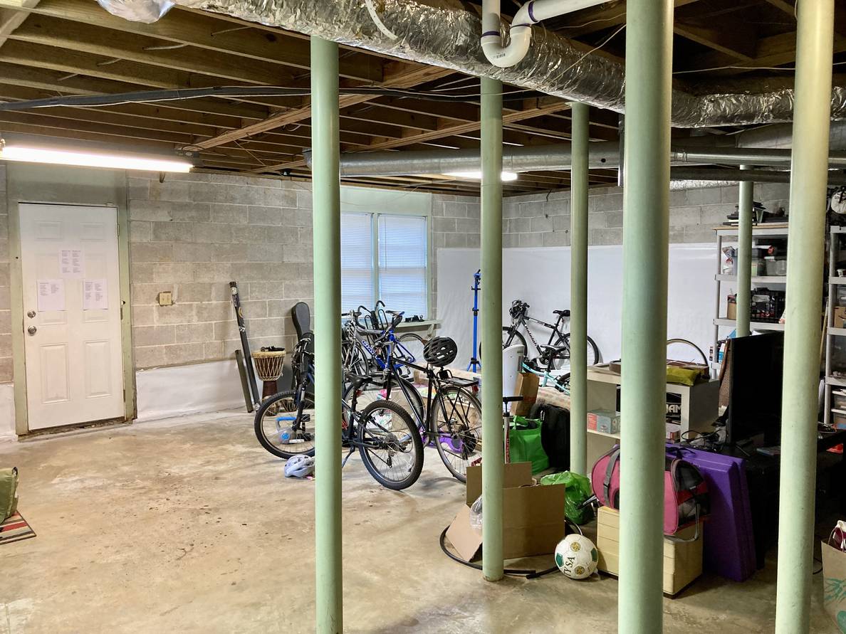 An unfinished basement with bikes, metal poles, stuff on the floor and on some shelves.