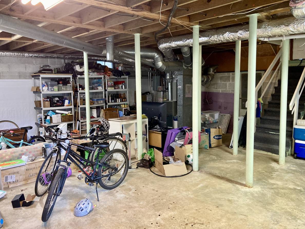 An unfinished basement with bikes, shelves of stuff, and stuff on the floor.