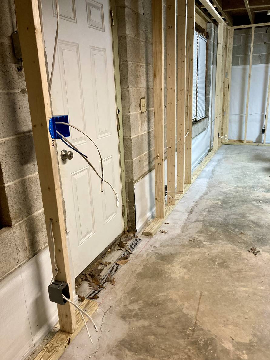 An unfinished basement with electrical boxes mounted to studs and cable coming out.