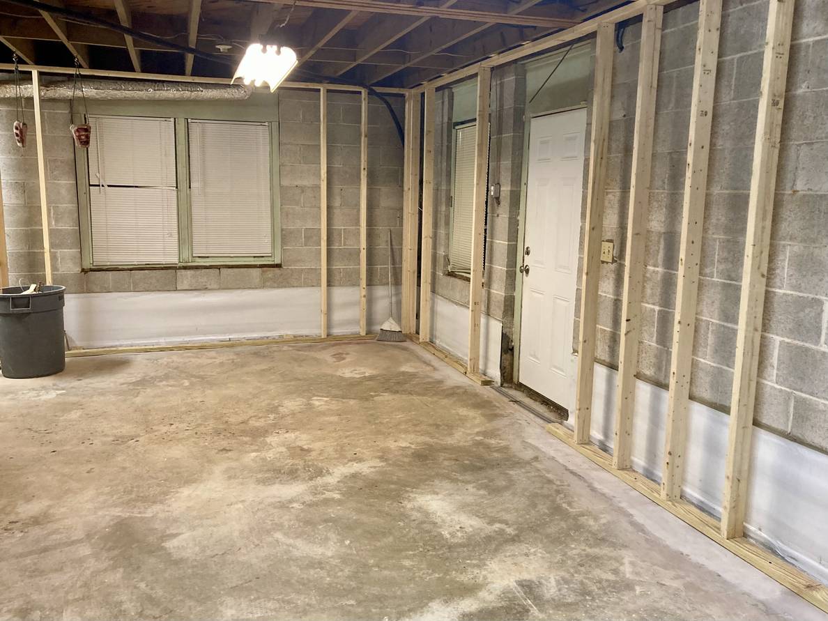 An unfinished basement with concrete walls lined with wooden studs