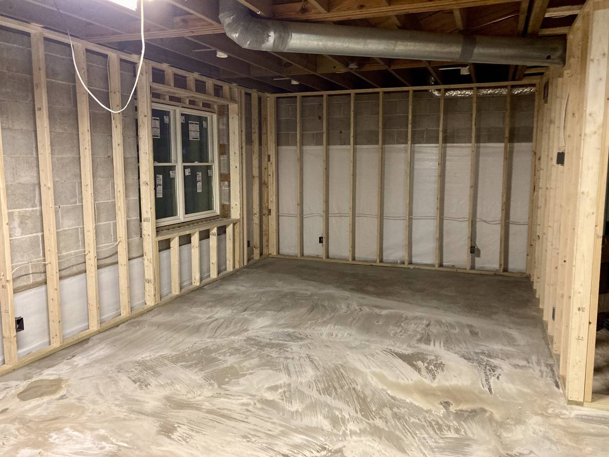 The main space of the basement. The floor is swirly from the floor leveler and a new window with stickers is on the far wall. The perimeter of the space is framed out.