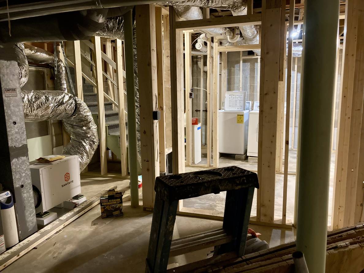 The utility room. The walls are framed out, the HVAC is visible with the new dehumidifier, and a framed doorway shows the laundry room across the stairway alcove.