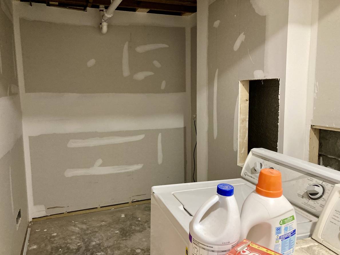 A photo of a partially finished laundry room with the walls drywalled and mudded