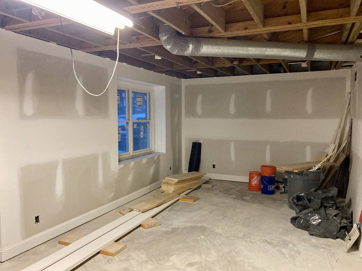 A photo of the main space of the partially finished basement. Some baseboard trim has been installed along unpainted walls.