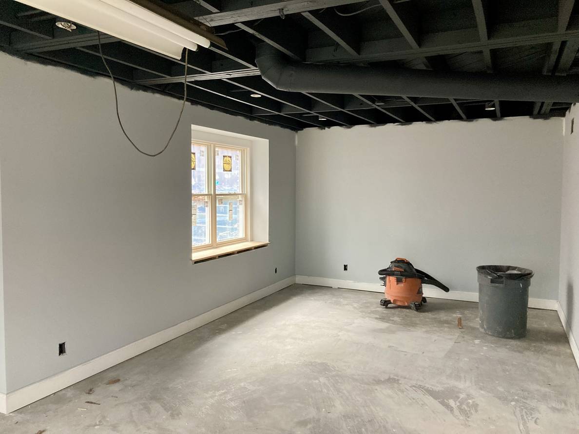 A photo of the main space of the basement. The ceiling has been painted a charcoal color and the walls are a gray color. A window is visible with an unfinished pine sill about a foot deep.