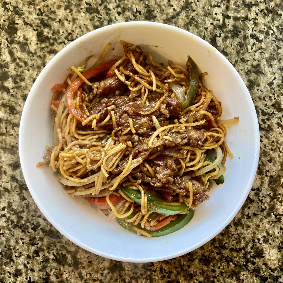 A photo of a bowl of Chow Mein with Beef and Peppers. Slices of beef, green and red bell peppers, and oniones are visible among the noodles.