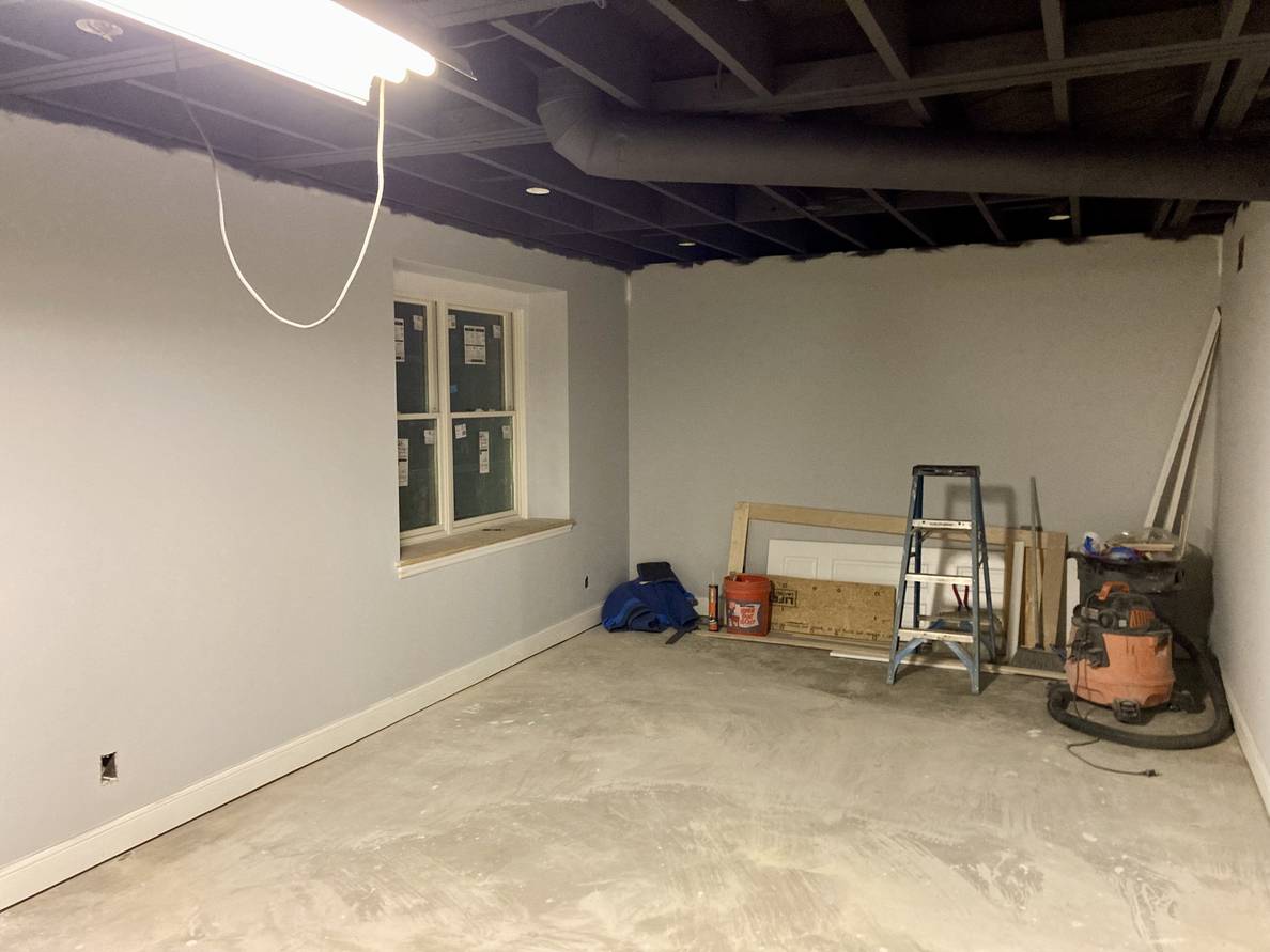 A photo of the main space of the partially finished basement. Against the far wall, among other tools and material, is the old stair door.