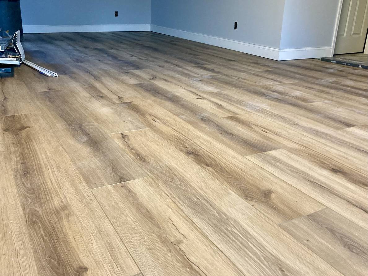 A photo of a partially finished basement floor. Almost all of the visible floor has wood-looking flooring installed.