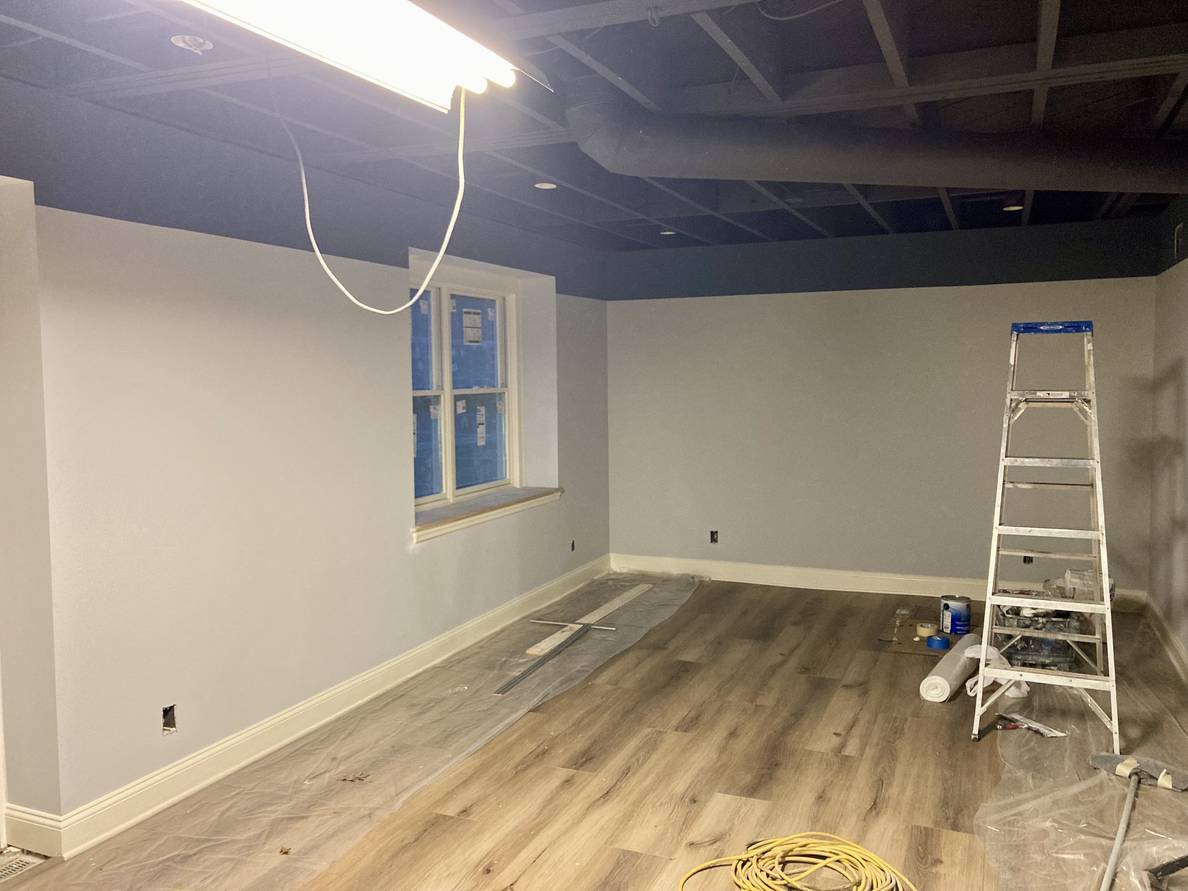 A photo of a mostly finished basement. Flooring is newly installed. The walls have a darker strip of color about 14 inches tall from where they meet the ceiling.