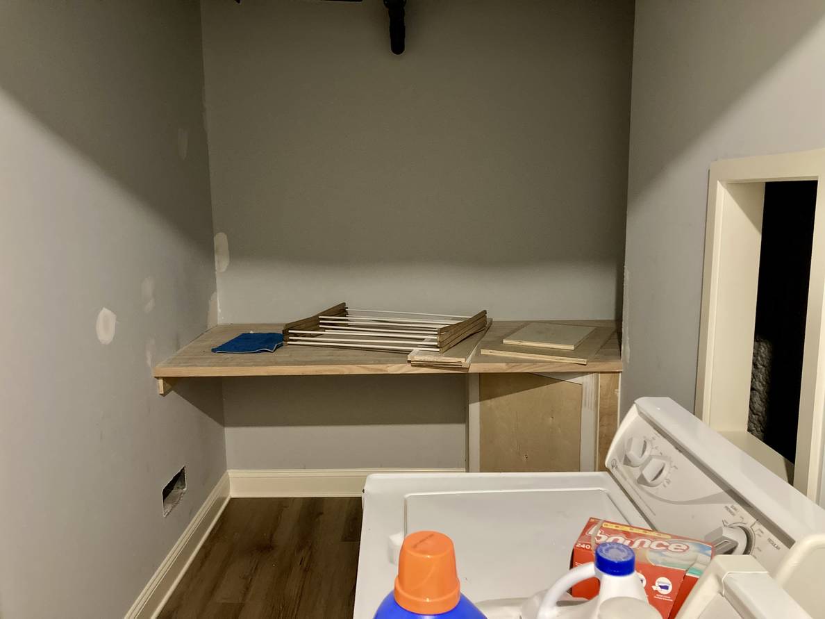 A photo of the partially finished laundry room. The laundry shelf is visible on the far end with a cabinet concealing the sump pump access.