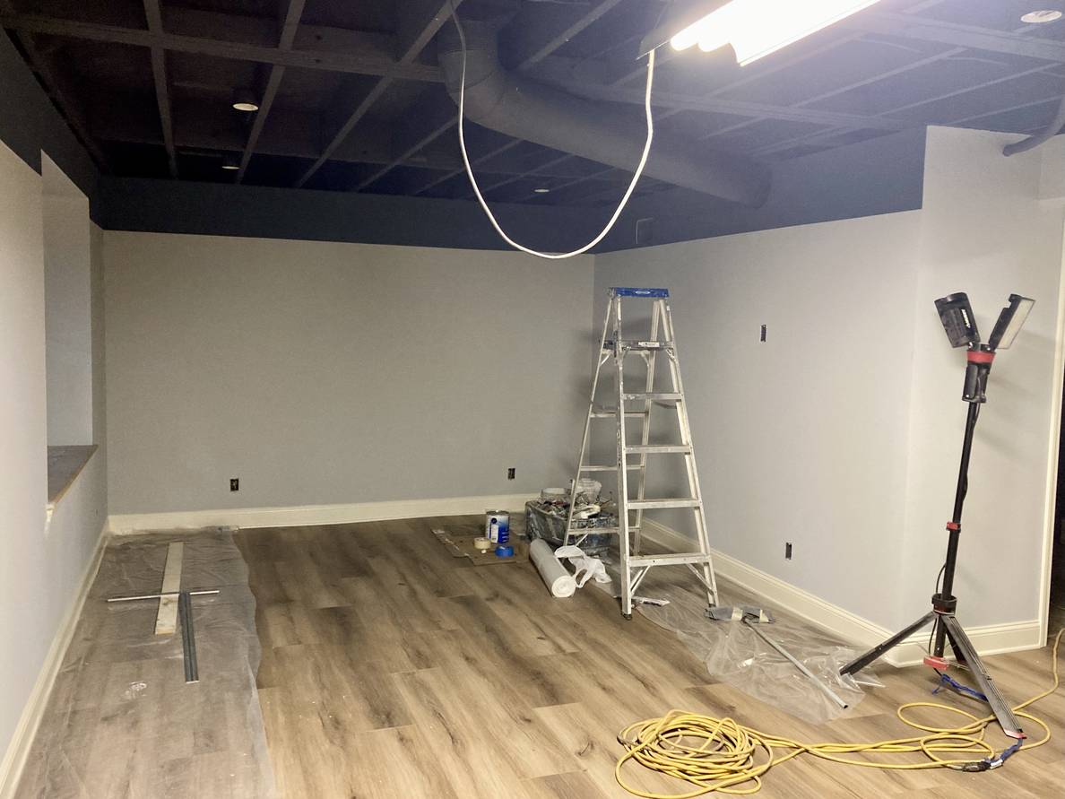 Another photo of the same basement from another angle. Painting supplies are still out, including a ladder and some pieces of plastic sheeting on the floor.