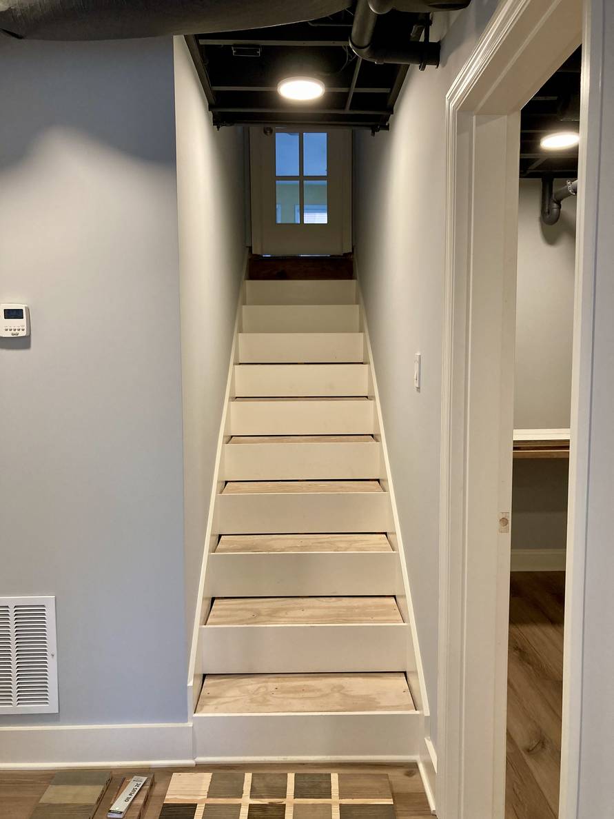 A photo of the stairs. The step treads are not yet installed. At the bottom of the stairs is a piece of wood with squares of stain that we used to see what we wanted to use for the tread stain.