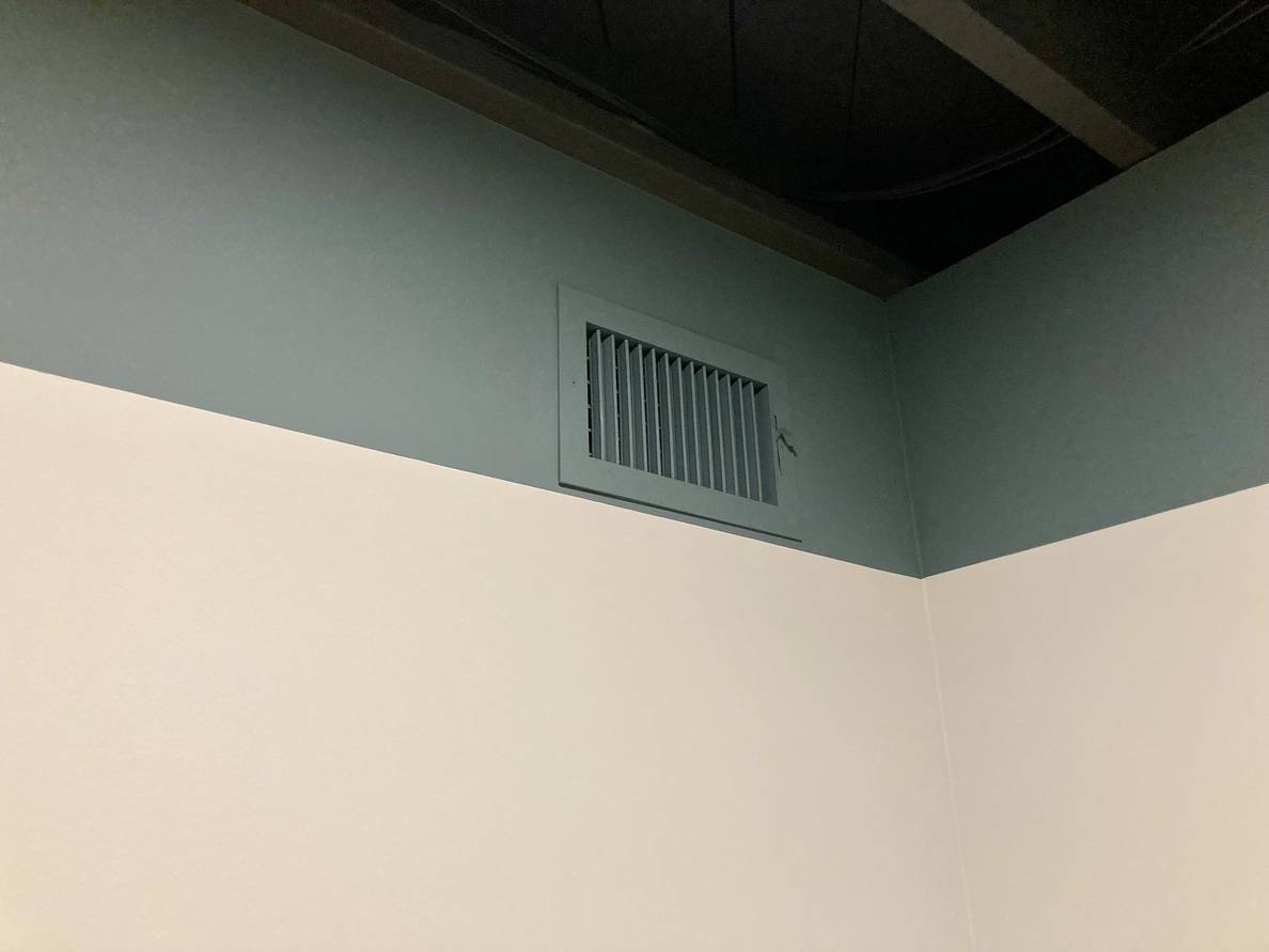 A photo of a two-toned wall. A ventilation grille is on the darker tone and has been painted the same color to match.