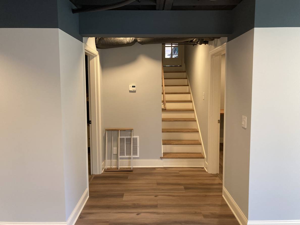 A photo of the finished stairs from the bottom, and the little alcove space at their foot. The doors to the utility room and laundry room open on either side of the alcove space.