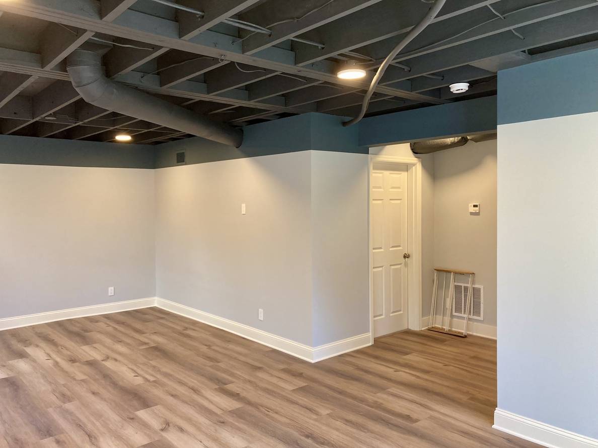 Another photo of the basement from the same position, but after the work has been done. The space is divided by walls and no metal poles are visible. Some of the poles have been removed, making an alcove towards the stairs.